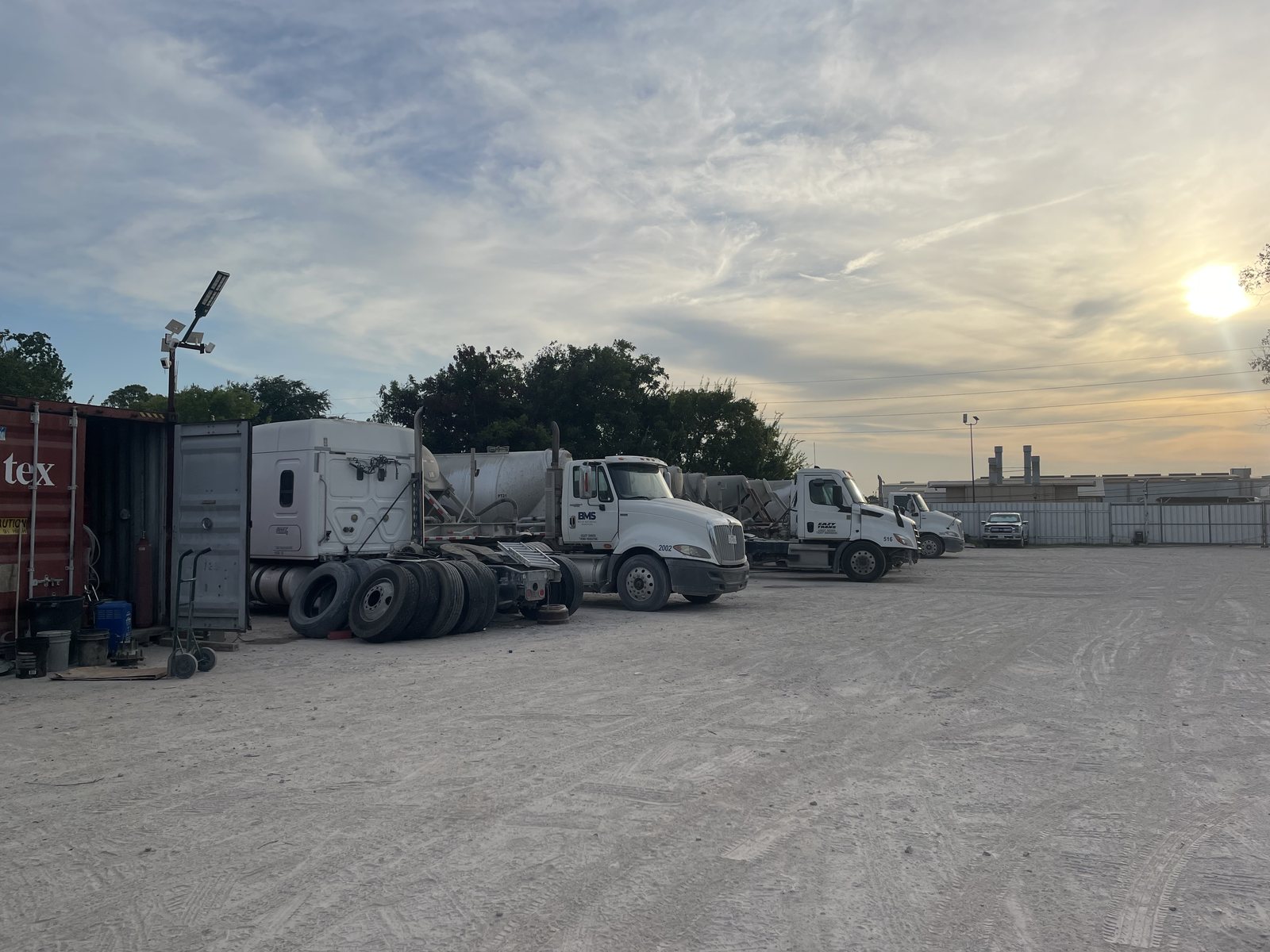 The fenced perimeter and solar lighting mast at the Eazy Trans Houston yard, with tractors and a parts container along the fence line